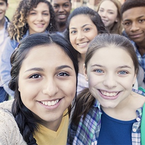 Diverse group of eight high school students are smiling and looking at the camera. Teenagers are students at public high school, and are wearing backpacks or holding school books.