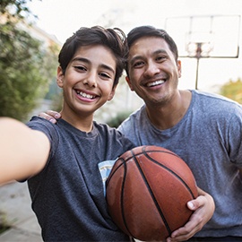 Hispanic-father-and-son-taking-a-selfie-outdoors-whilst-playing-basketball-1130685992_6016x4016