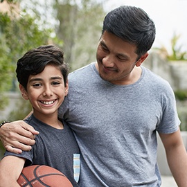 Portrait of happy boy and father with basketball Portrait of happy boy standing with father at basketball court. Mid adult man and child are smiling in backyard. They are in casuals during weekend.