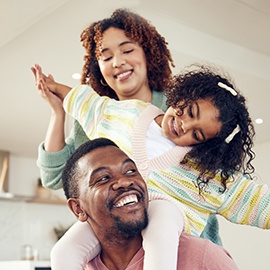Black family, father and daughter playing with mother on living room sofa together for fun bonding at home. Happy dad carrying child for piggyback ride with mom on lounge couch enjoying holiday break