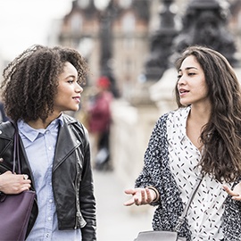 Two young women walking in Paris street having conversation. Young woman gesturing with hands, female friend listening