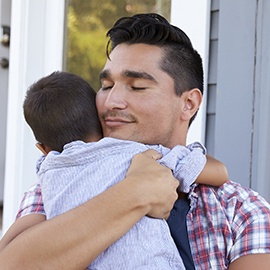 Father Hugging Son Sitting On Steps Outside Home